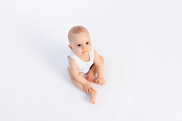 cute baby boy in a white bodysuit on a white isolated background looks at the camera, baby 8 months, children's fashion, advertising children's clothing, space for text