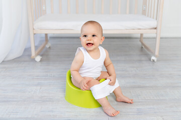 small baby boy 8 months old sitting on a green potty, baby toilet, place for text