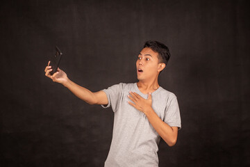 Wow face of Young Asian man shocked and surprised what he see in the smartphone. Indonesian man wearing gray shirt.