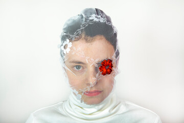 Portrait of young woman wearing white veil with red flower covering one eye