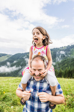 Happy father carrying daughter on shoulders on a meadow in the mountains, Achenkirch, Austria