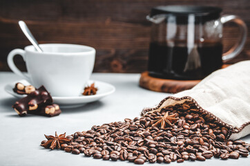 roasted coffee beans are scattered from a bag on a stone light background with a Cup and a glass coffee pot, selective focus with a small depth of field coffee beans