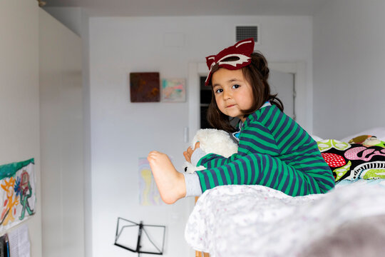 Portrait of little girl with fox mask sitting on barefoot bunk bed at home