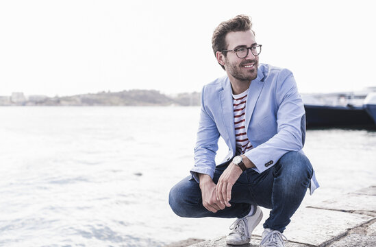 Smiling young man crouching on the waterfront