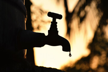 Silhouette of old vintage metal tap leaking last water droplet. alone in outdoor natural...