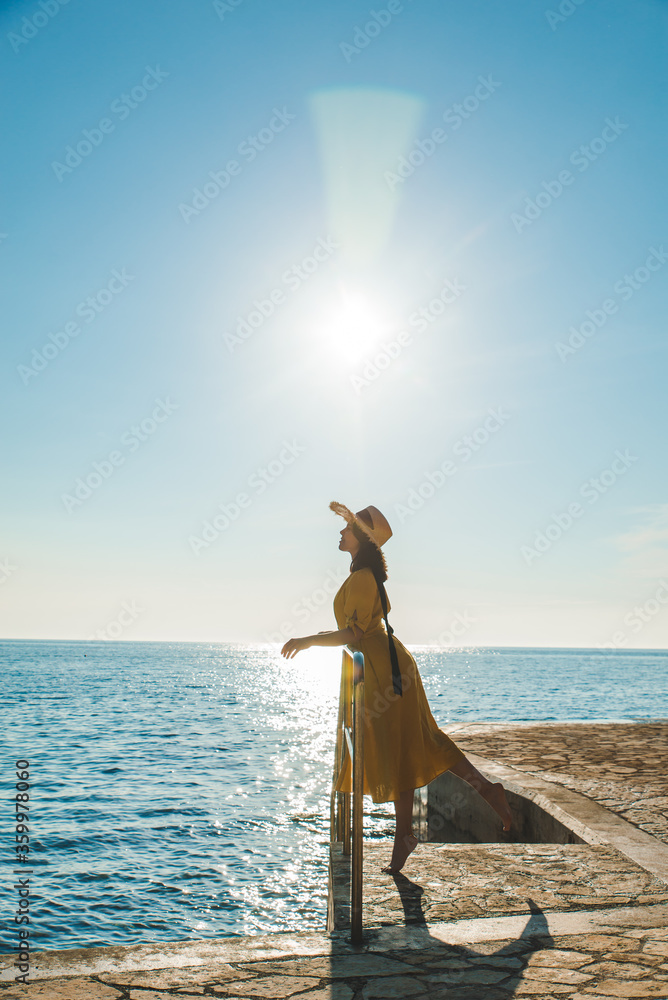 Wall mural young pretty woman in yellow sundress at sea beach