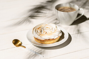 Lemon meringue little pie on a wooden board, table on a palm beach outdoor cafe in the shadows of palm branches. Continental breakfast with a cup of coffee.