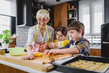 Grandmother baking cookies with her grandchildren at home. Baking cookies. Happy grandmother with her grandchildren having fun