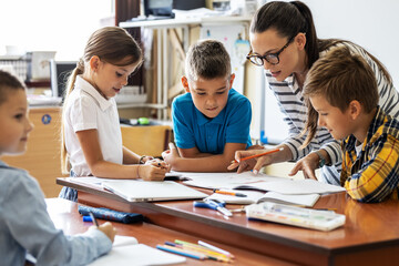Female teacher helps school kids to finish they lesson.They sitting all together at one desk.