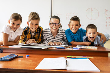 Portrait of primary school kids with they female teacher.They sitting at the desk in classroom.