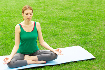 A woman practices yoga outdoors on the grass. Copy space