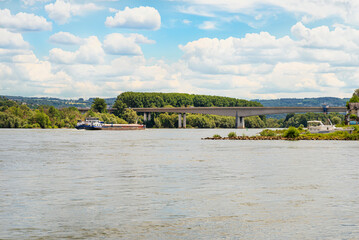 Concrete road bridge on the highway over the river in western Germany, visible flowing cargo barge, in the background blue sky and clouded clouds