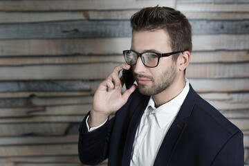 Male economist talking on cell telephone while standing in modern interior with copy space area, young successful men entrepreneur speaking on mobile phone during work