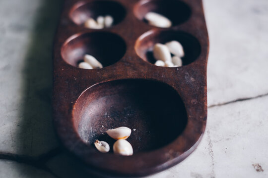 Closeup of head part of Sungka, Philippine mancala game, on off-white marble stone table with seashells pieces. Selective focus.