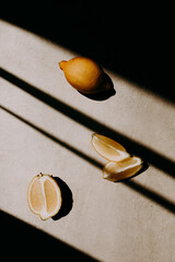A whole, a half and two quarters of lemon on grey background with shadow stripes and lines. Harsh...
