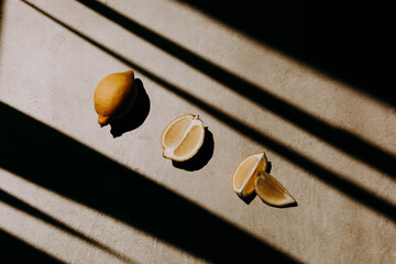 A whole, a half and two quarters of lemon on grey background with shadow stripes and lines. Harsh...