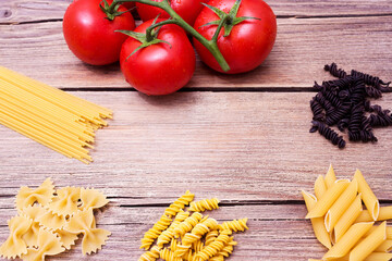 Different pasta and tomatoes on a wooden background