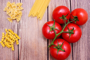 Different pasta and tomatoes on a wooden background