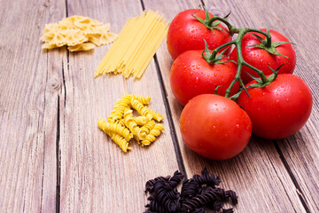 Tomatoes and different pasta on a wooden background