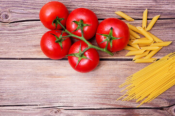 Bunch of raw spaghetti with a truss of tomatoes in a rustic scene