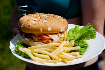 the girl holds a plate with a hamburger and fries and a glass of soda