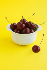 Red cherries in the white bowl on the yellow background. Location vertical. Copy space.