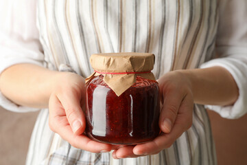 Woman holds glass jar with strawberry jam, close up
