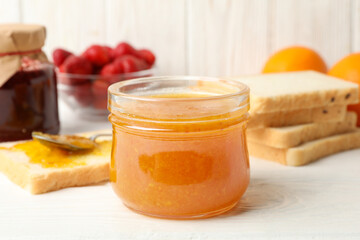 Composition with apricot jam on white wooden background. Sweet breakfast