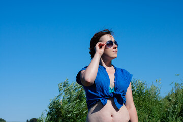 a young sexy woman in a swimsuit and a blue shirt adjusts her sunglasses. in summer