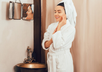 Fototapeta na wymiar Pretty woman with towel on head wearing bathrobes standing near shower after spa procedures. Woman, after taking shower