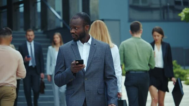 Busy african american business guy corporate executive surfing the internet on smartphone social media walking outdoors on office break. Successful people lifestyle.