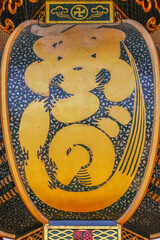 tokyo, japan - march 31 2020: Close-up on a huge japanese copper lantern hung in the Senso-ji temple of Asakusa with a gold engrave of a manji buddhist swastika and ideograms of uogashi or fish market