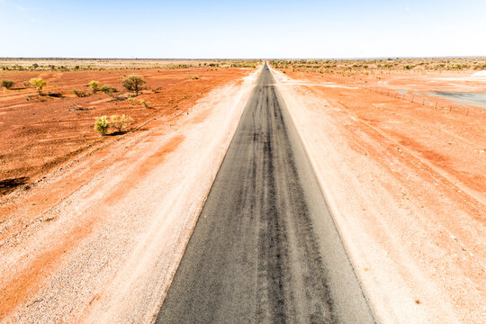 A rural highway straddled by dry red earth.
