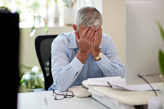 Mature business man sitting at a desk in a studio, thinking, worried