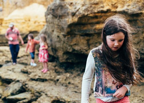 Girl carrying shells, family in background. Exploring limestone beach