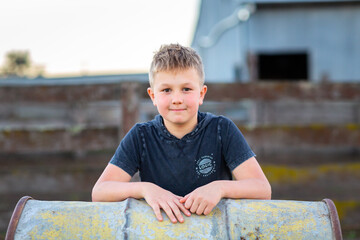 Fair haired boy leaning on a drum on a farm