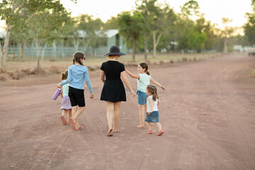 Woman and children walking away down dirt road from behind