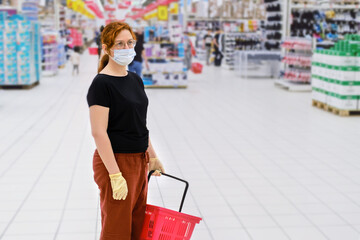 An adult woman in a medical mask stands in the middle of an empty hypermarket. Shopping at a supermarket. Being in public places during the epidemic of the coronavirus