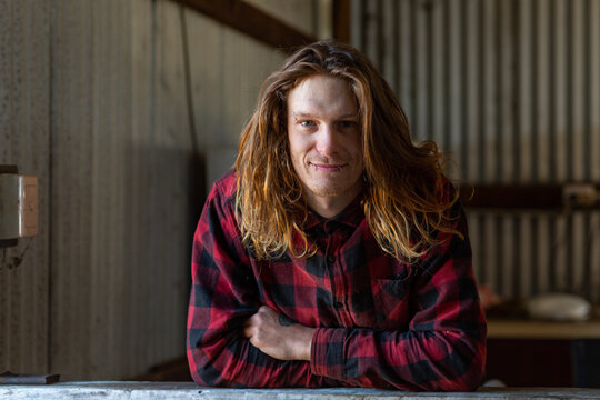Portrait of young man in flannel shirt leaning on bench in shed