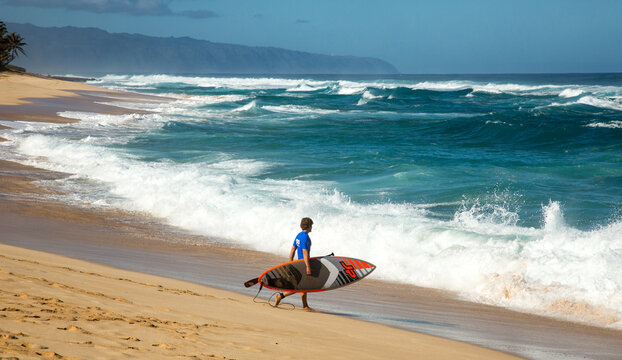Oahu, Hawaii, one man with a surfboard on the beach preparing to surf on the north shore pipeline