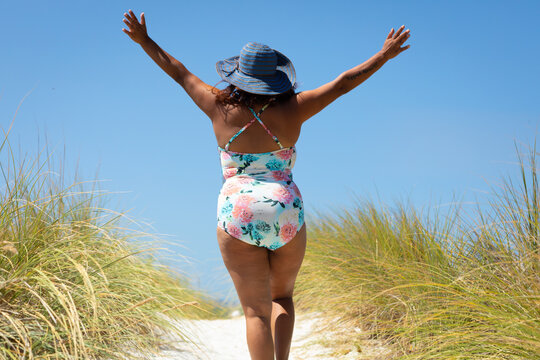 woman walking on dune path with arms raised in exultation