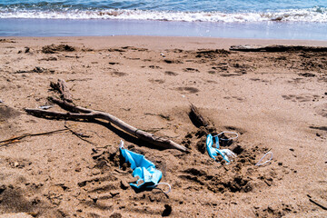Fototapeta na wymiar Medical face masks used and thrown on the floor of an empty beach. Covid coronavirus contamination in the sea.