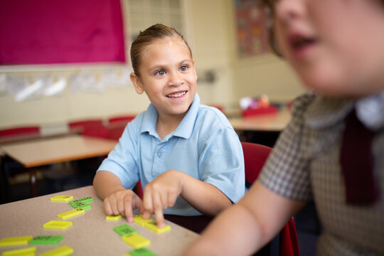 Indigenous girl primary school student sitting smiling at her friend working with word tiles