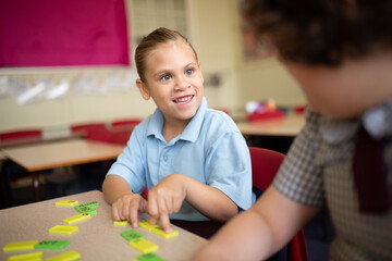 Indigenous girl primary school student sitting smiling at her friend working with word tiles