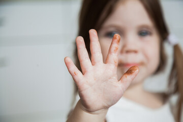 Little girl holding out sticky chocolate fingers to camera