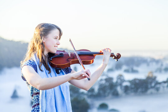Violin player standing out on cliff top playing music on misty morning