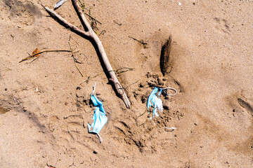 Used medical masks discarded on the sand of an empty beach. Covid coronavirus contamination.