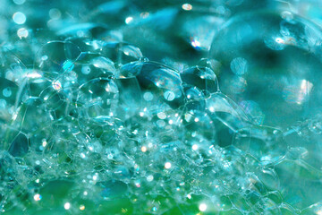 Close up photo of blue-green transparent soap bubbles and foam. Abstract background, selective focus, defocused image, bokeh backdrop.