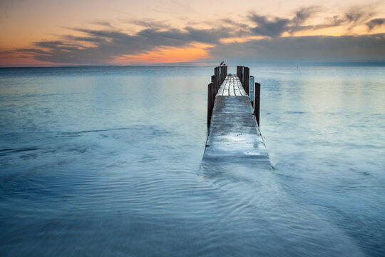 Looking along a wet wooden jetty toward a dawn sky.