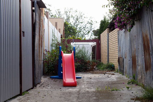 A small red childrens slide in an alleyway